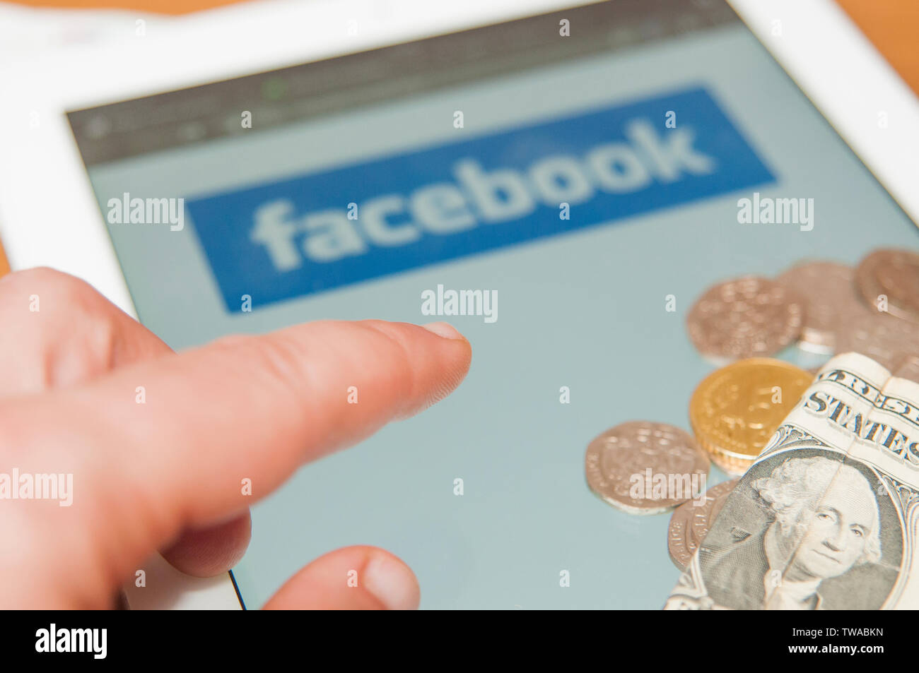 CARRARA, Italia - 19 giugno 2019: mano prendere soldi da un grappolo di moneta su un notebook con il logo di Facebook. Facebook annuncia il nuovo global cryptocurrency calle Foto Stock