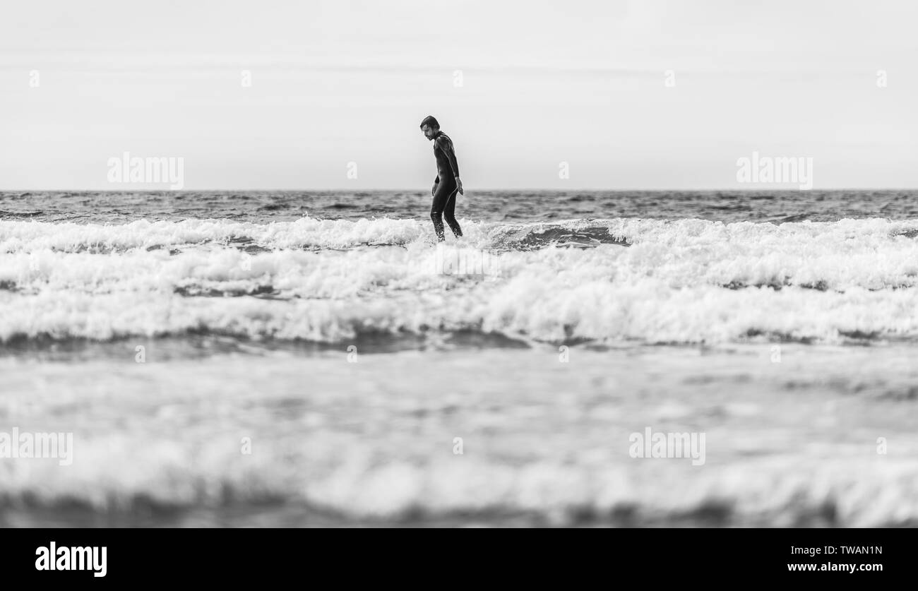 Surfer guy surf con la tavola da surf sulle onde in oceano Atlantico. Uomo in surf muta è attiva la navigazione in ondate di freddo oceano atlantico in Galizia, S Foto Stock