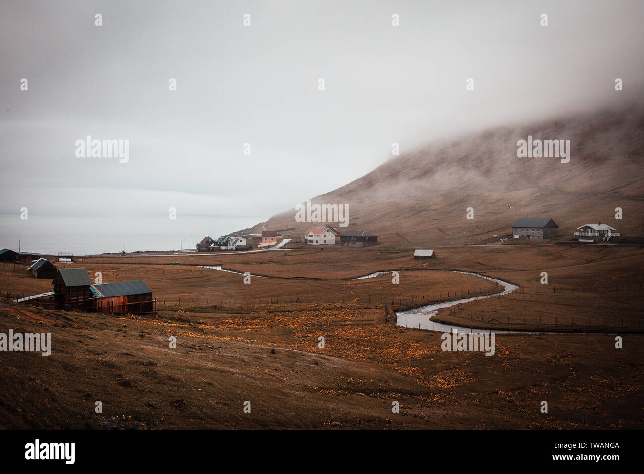 Il fiume di avvolgimento e solitario villaggio costiero avvolta nella nebbia sulle Isole Faerøer. Foto Stock