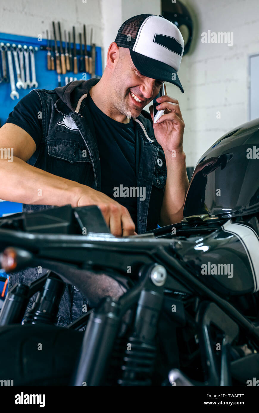 Mechanic parlando telefono mentre il fissaggio moto Foto Stock