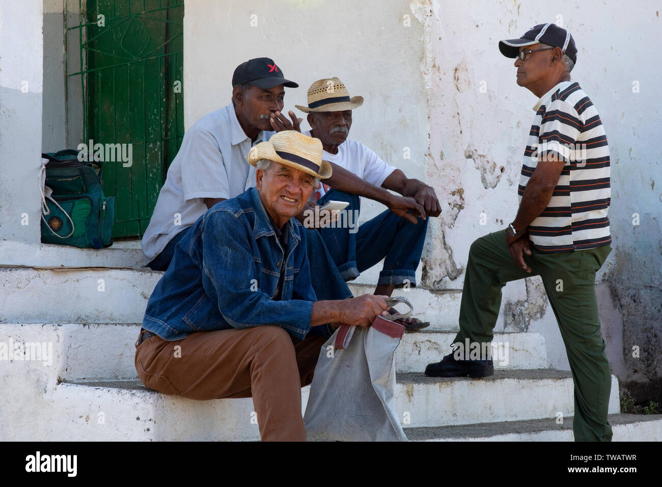 Un gruppo di uomini cubani seduti e chiacchierare al di fuori di un cubano di razionamento alimentare shop a valle presso la Valle de los Ingenios, tra Cienfuegos e Trinid Foto Stock