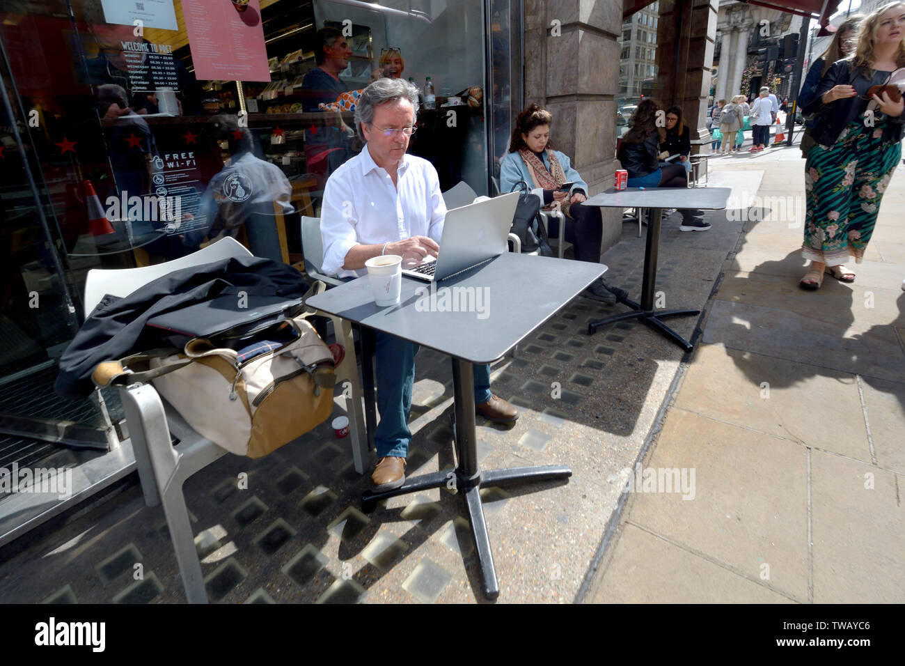 Londra, Inghilterra, Regno Unito. La gente seduta al cafe esterno tavoli in Piccadilly. L'uomo sul suo computer portatile Foto Stock