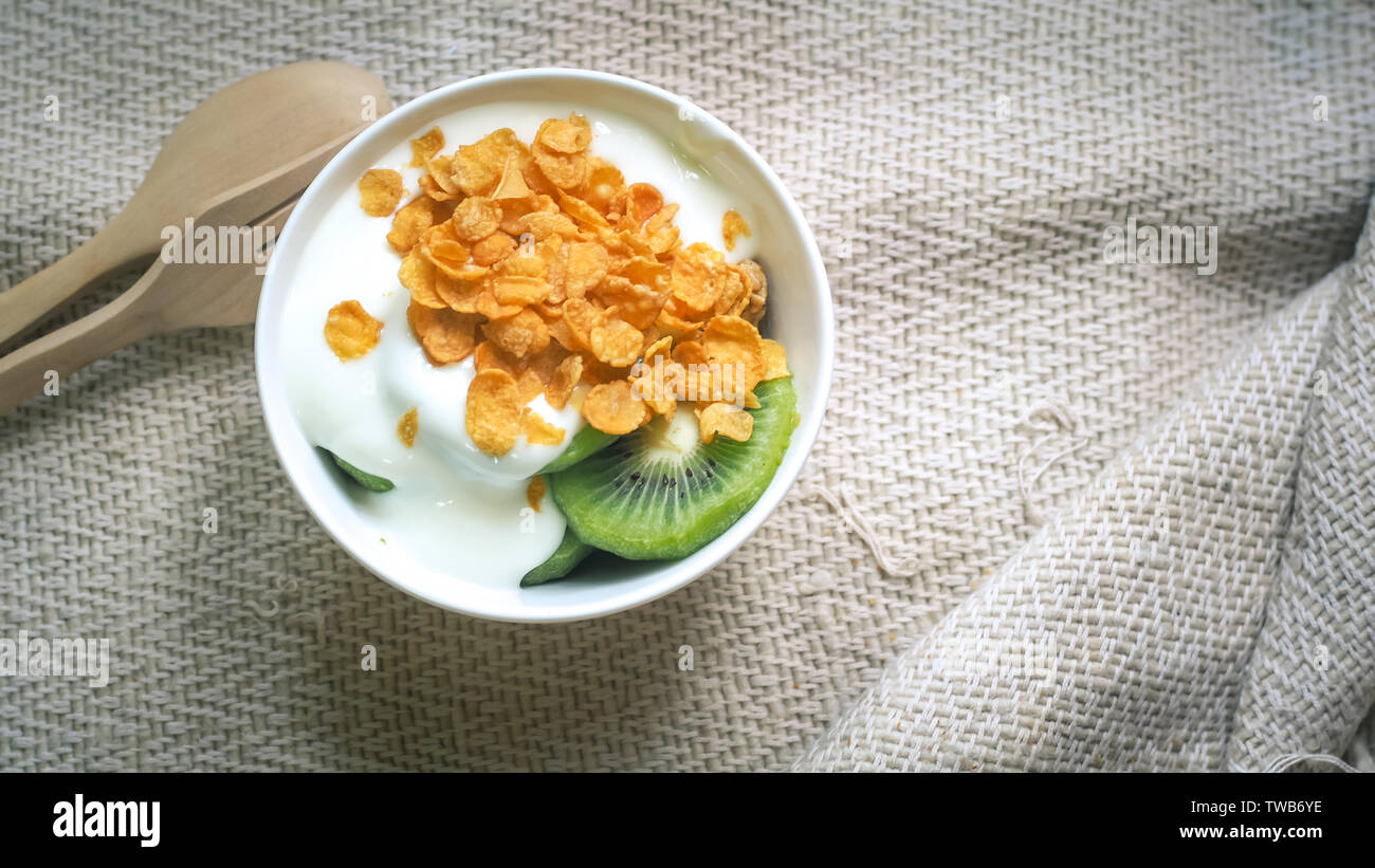 Fiocchi di mais, cereali e latte splash in ciotola. In casa naturale plain yogurt biologici in ciotola di legno su legno sfondo texture Foto Stock