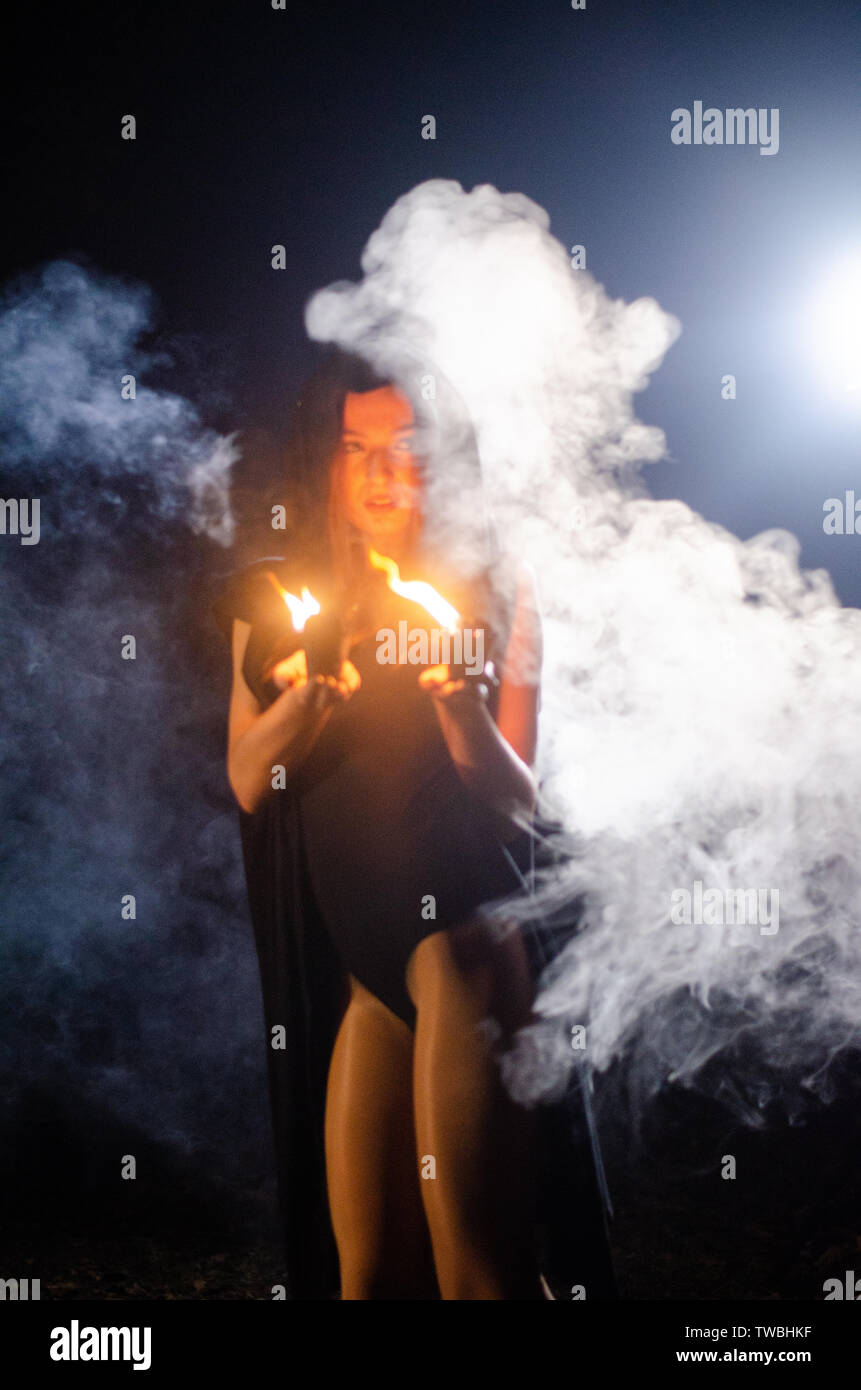 Giovane ragazza in un lungo mantello nero fuoco di notte. Foto Stock