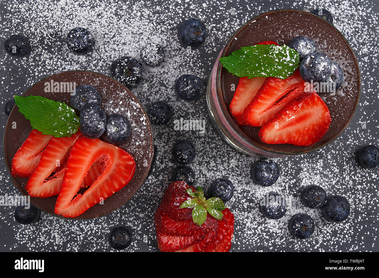 Mousse di ciliegio con biscotti sbriciolati, ciliegie sciroppate, ananas panna e cioccolato. Decorate con fragole, mirtilli e foglie di menta Foto Stock