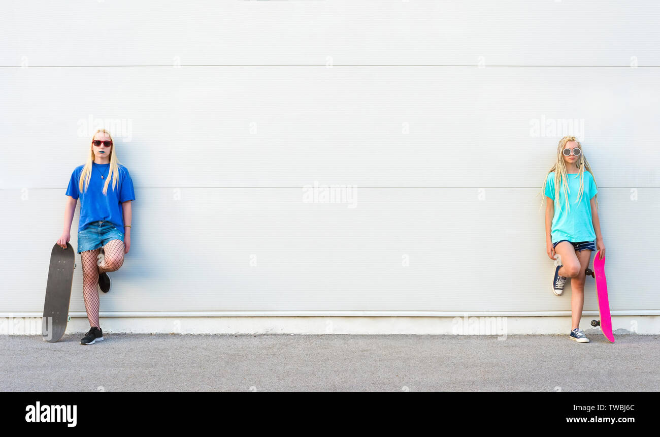 Due giovani donne skateboarders appoggiata al muro bianco Foto Stock