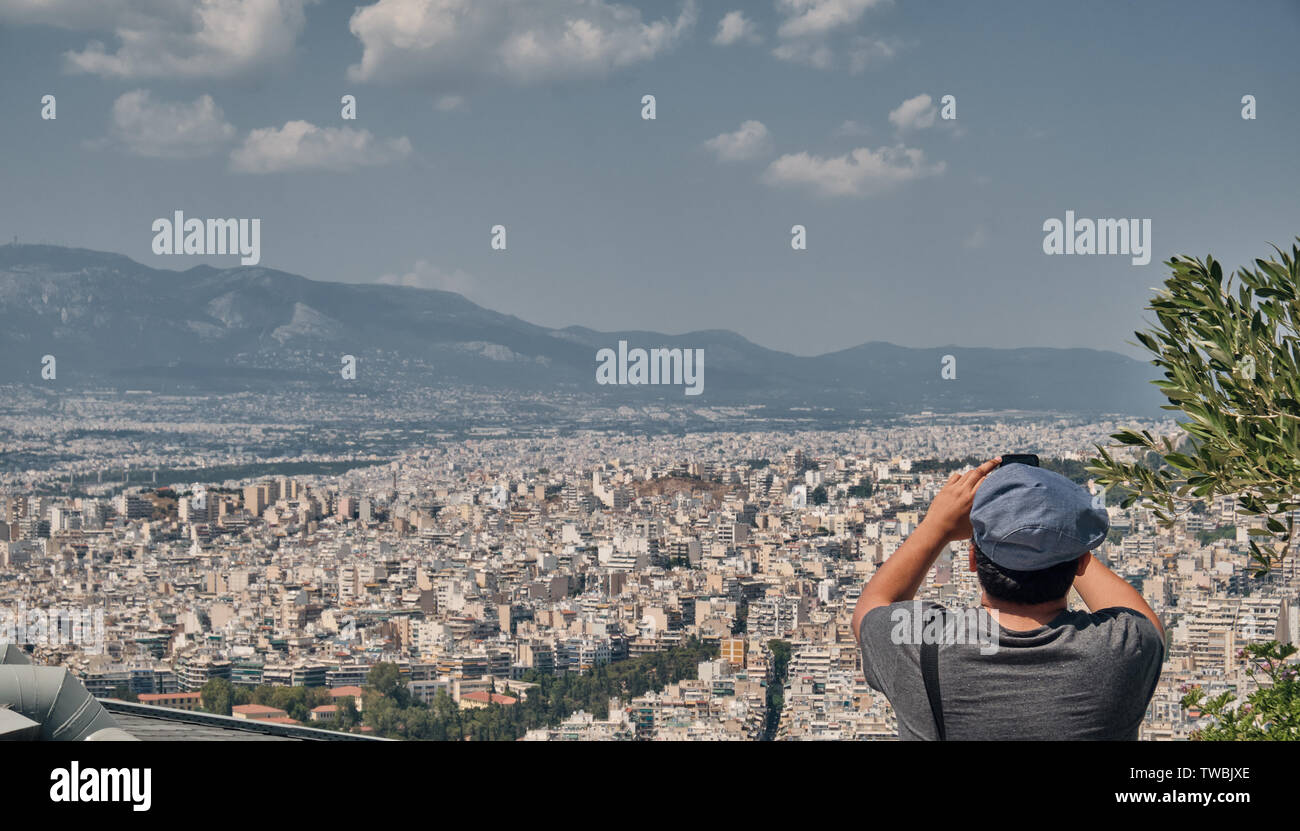 Uomo o ragazzo con smart-phone prendendo foto presso la città di Atene dal Monte Lycabettus in una giornata di sole Foto Stock