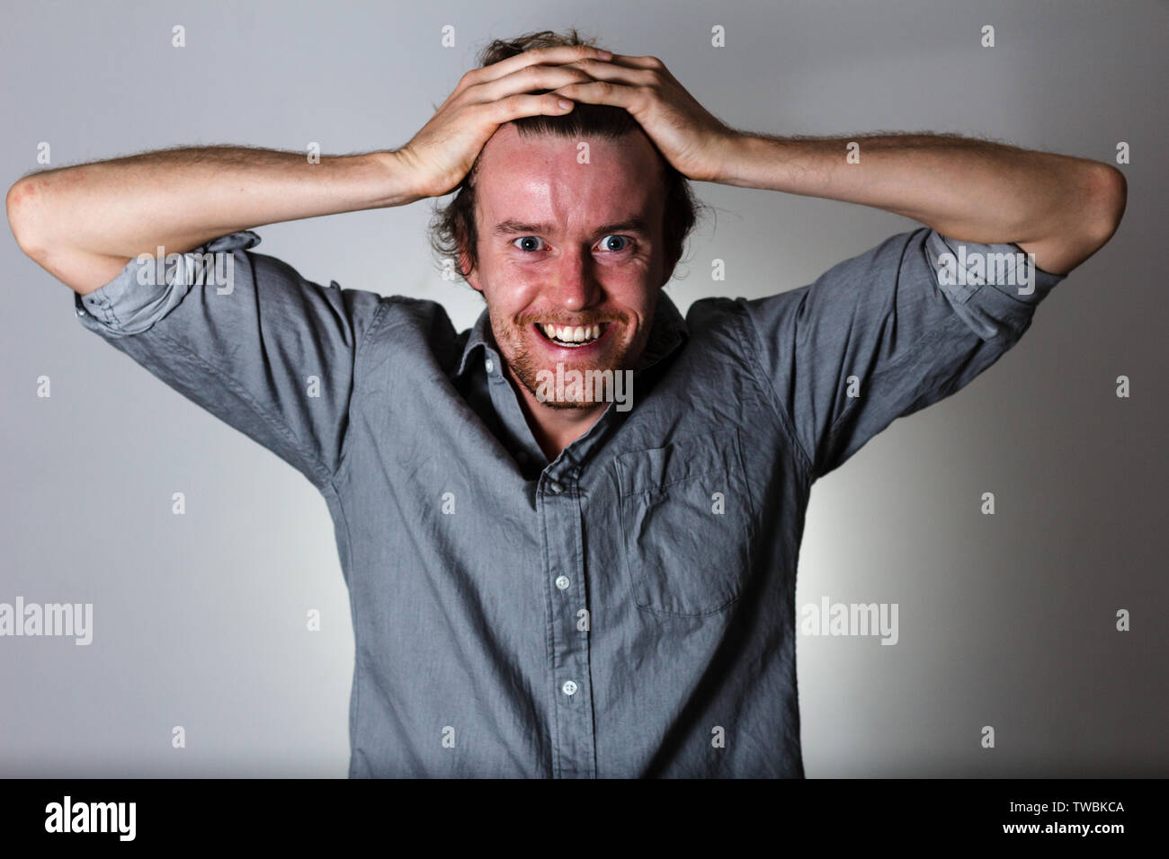 Scary crazy espressione del giovane uomo su sfondo grigio Foto Stock