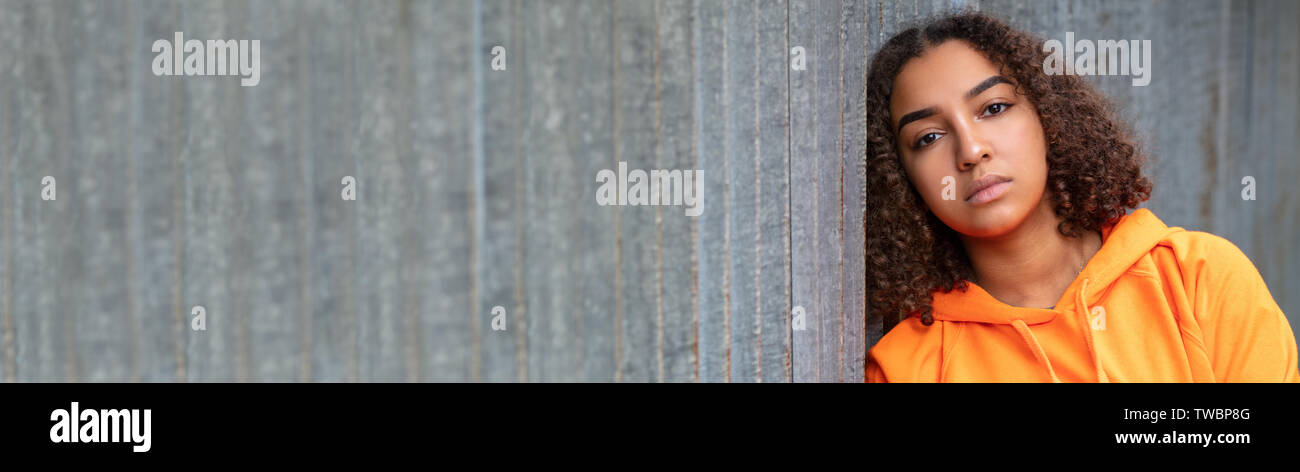 Panoramica banner web della splendida razza mista biracial americano africano ragazza adolescente femmina giovane donna al di fuori di indossare una felpa con cappuccio arancione cercando triste d Foto Stock