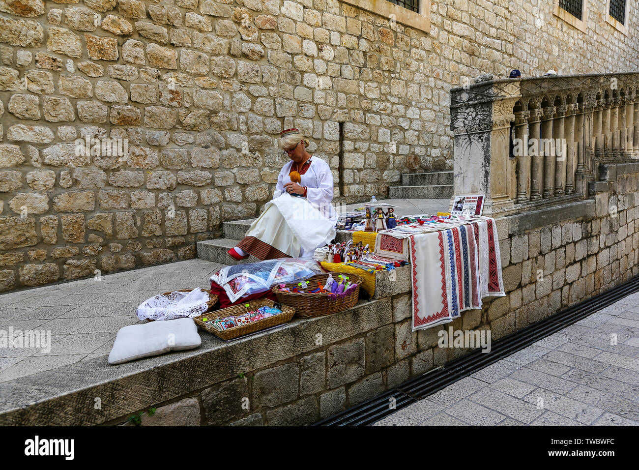 Una donna croata in abito tradizionale rendendo negozio di souvenir sulle mura della città di Dubrovnik, Croazia Foto Stock