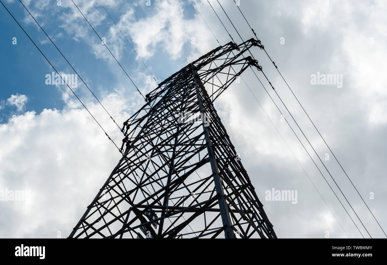 Vista dal basso di una di elettricità ad alta tensione pilone contro il cielo blu con nuvole a giornata di sole. Di potenza ad alta tensione torre di trasmissione. Ingegneria energetica. Foto Stock