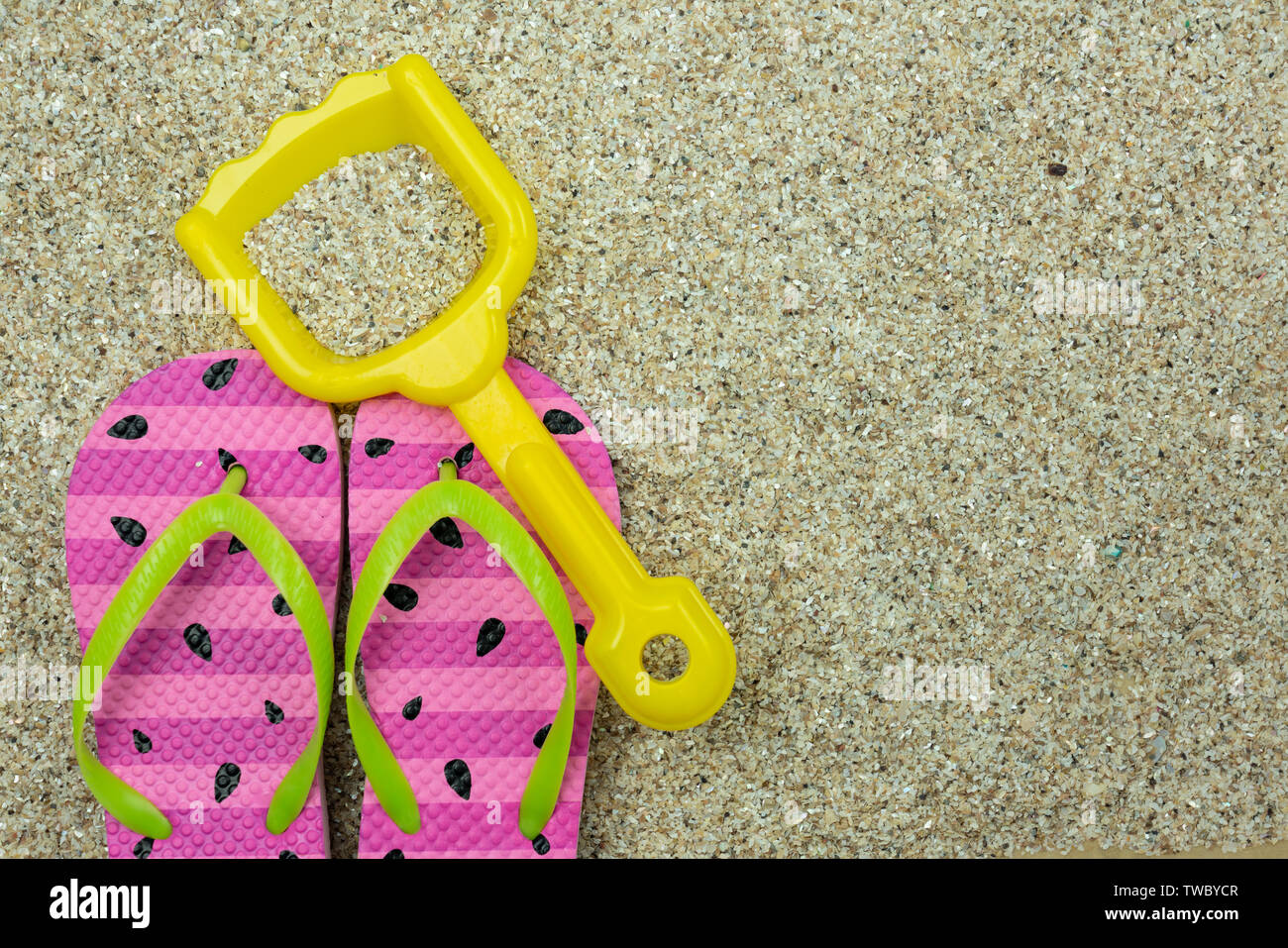 Divertimento al sole concetto con pattern di anguria childs flip flop sulla spiaggia in sabbia con una pala di giallo Foto Stock