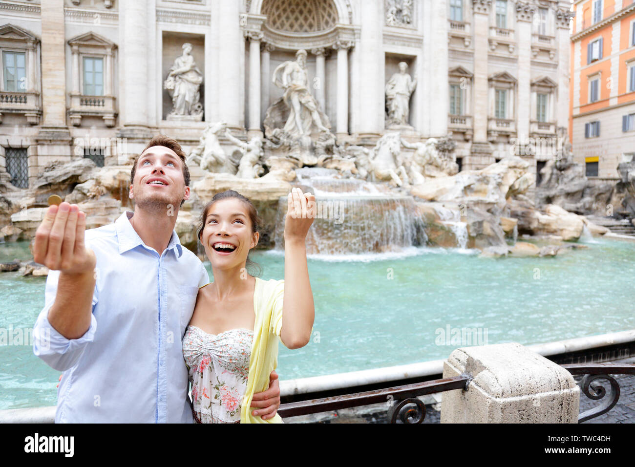 Viaggiare giovane trowing moneta alla Fontana di Trevi, Roma, Italia per buona fortuna. Felice coppia giovane sorridente che viaggiano insieme sul viaggio romantico casa vacanza in Europa. Donna asiatica, uomo caucasico. Foto Stock