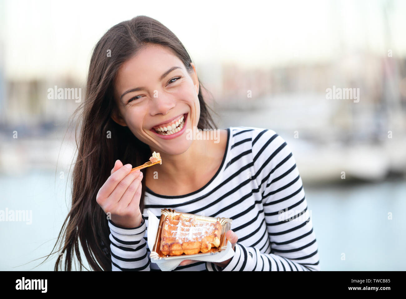 Waffle - donna mangiare waffle felice all'aperto sorridente ridere guardando la fotocamera. Bella ragazza a mangiare cibo snack al di fuori. Foto Stock