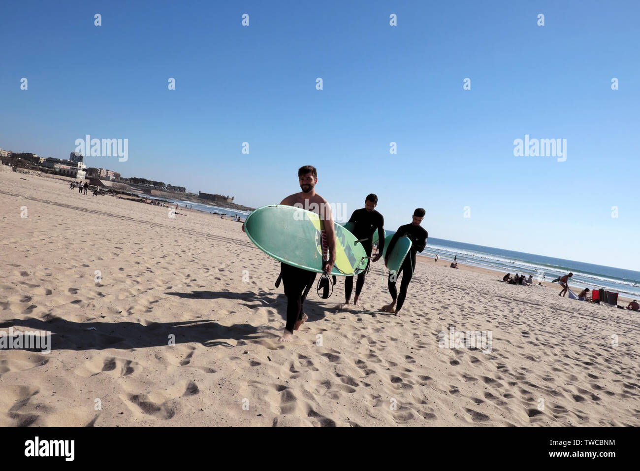 Giovani uomini che trasportano le tavole da surf in sole primaverile di camminare sulla spiaggia di sabbia a Matosinhos Porto Portogallo Europa KATHY DEWITT Foto Stock