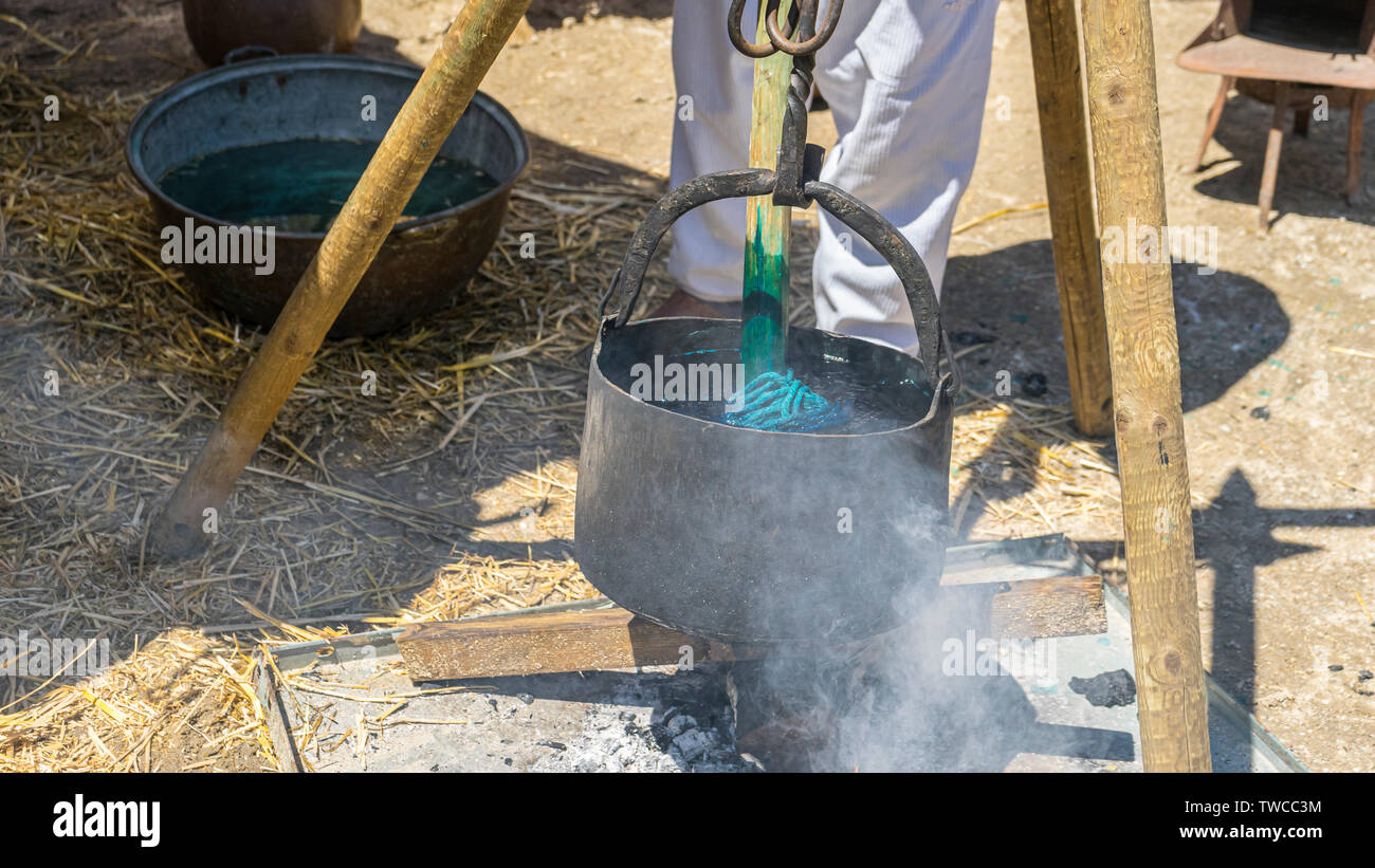 Artigianale di tintura dei tessuti di lana e in un calderone con pigmenti colorati in una fiera medievale in Spagna Foto Stock