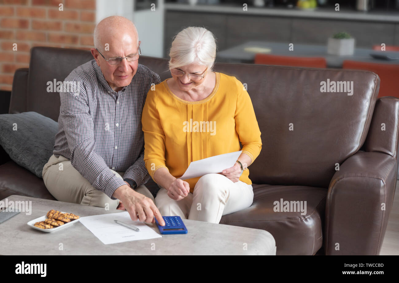 Coppia senior il pagamento di fatture insieme con la calcolatrice. Giovane facendo alcune pratiche e calcoli a casa Foto Stock