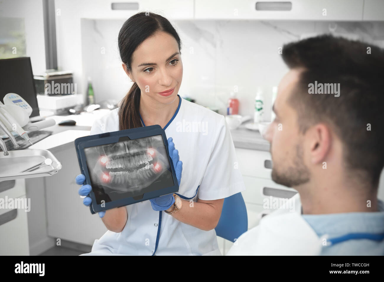 Dentista femmina mostra denti x-ray su tavoletta digitale sullo schermo. Paziente seduto su una sedia in professional dental clinic. Foto Stock