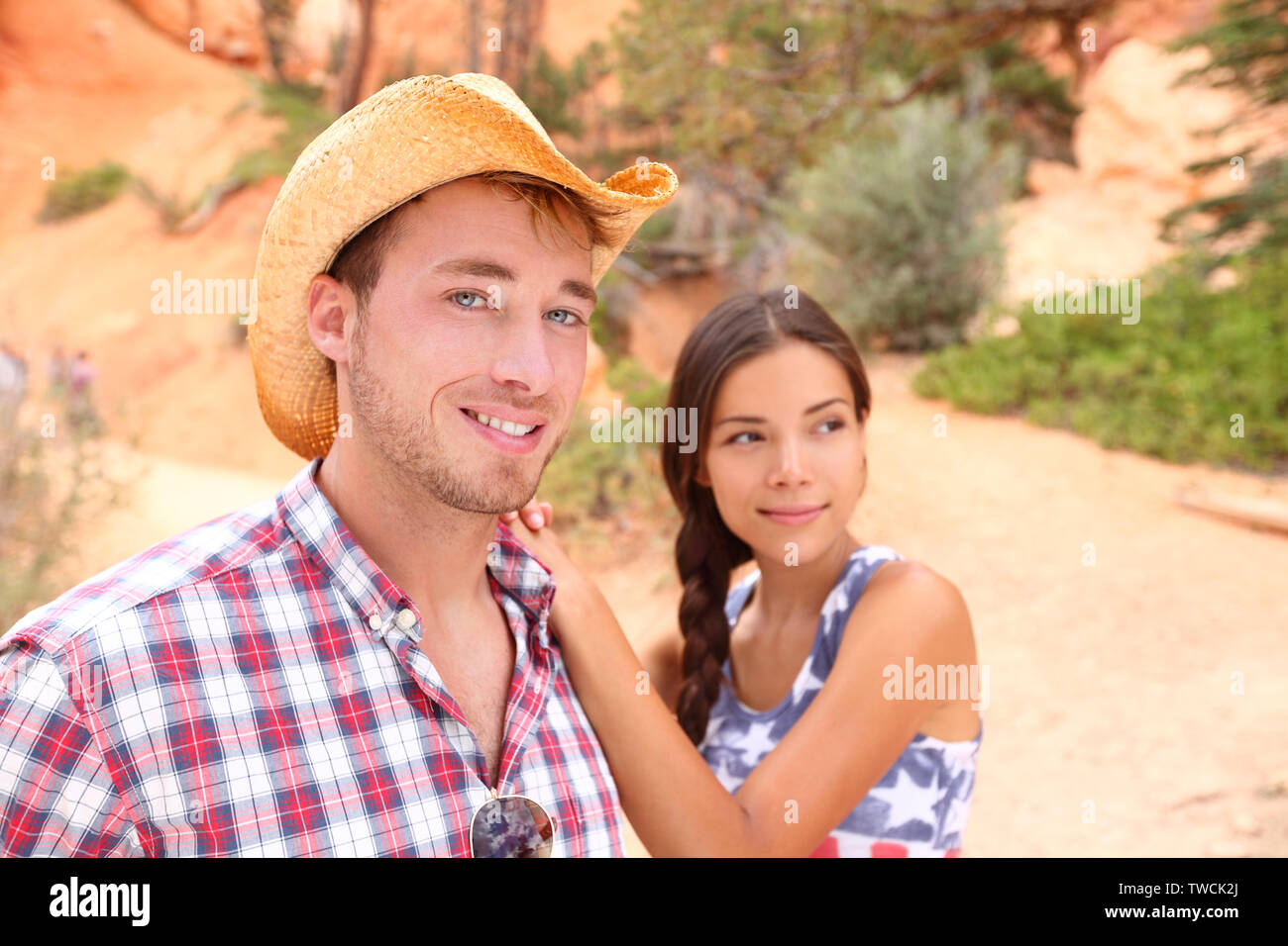 Giovane ritratto nella campagna americana all'esterno. Sorridente multirazziale coppia giovane in western USA la natura. Uomo che indossa il cappello da cowboy e la donna che indossa bandiera degli Stati Uniti maglietta. Foto Stock