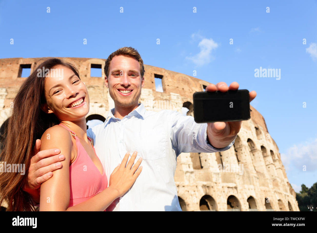 Accoppiare lo smartphone che mostra a Roma dal Colosseo in Italia. Felici gli amanti in luna di miele sightseeing Coliseum. Amore e concetto di viaggio con multirazziale giovane. Foto Stock