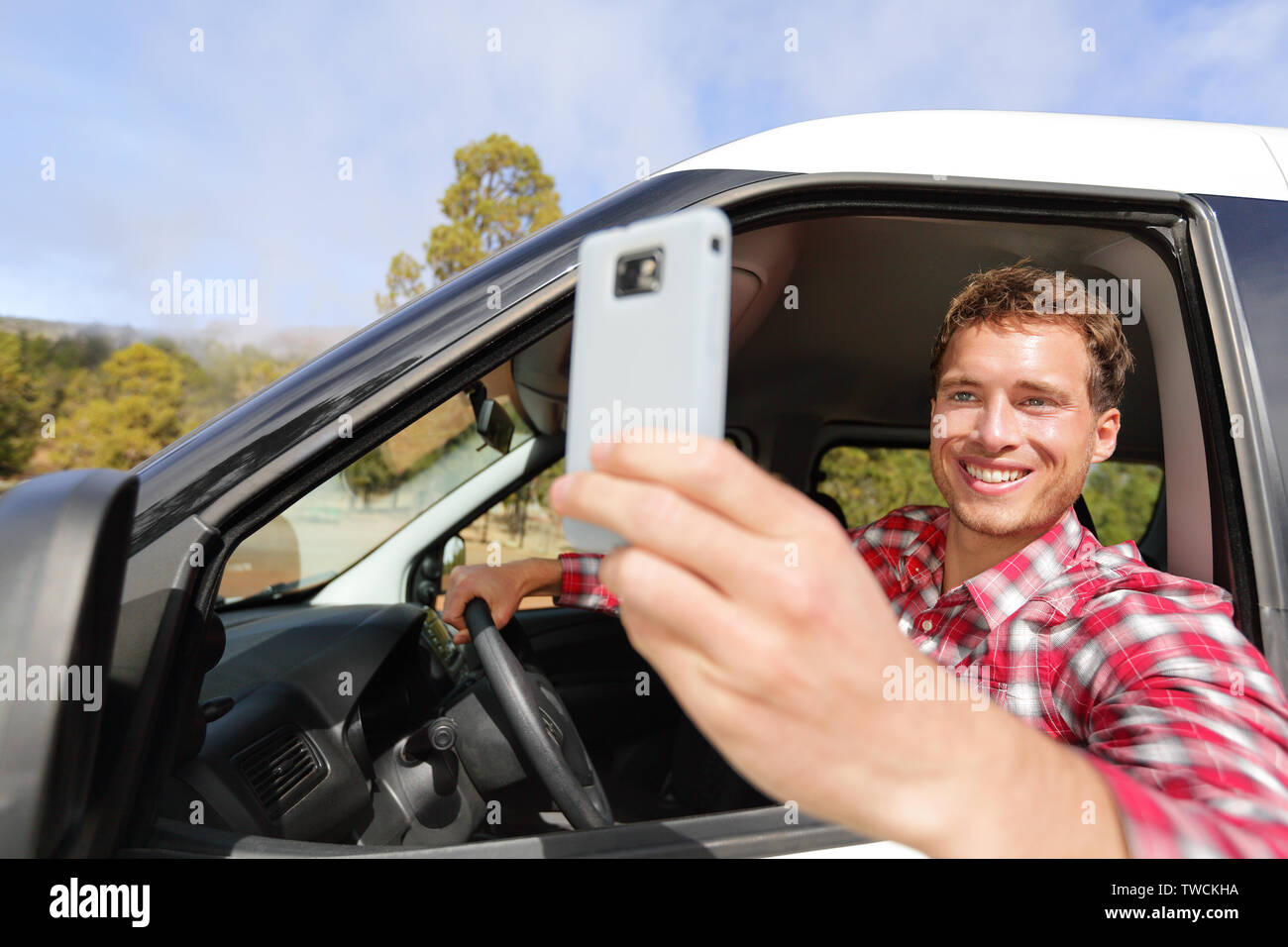 Conducente di prendere foto con la fotocamera dello smartphone in guida auto. Uomo felice di prendere foto con smart phone fotocamera finestra della vettura durante i viaggi viaggio su strada. Giovani caucasici modello maschio nel suo 20s. Foto Stock
