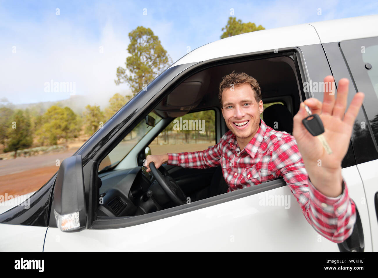 Auto nuove - uomo alla guida di auto che mostra le chiavi dell'auto felice guardando la fotocamera. Driver maschio sul viaggio nel bellissimo paesaggio naturale. Focus sul modello. Foto Stock