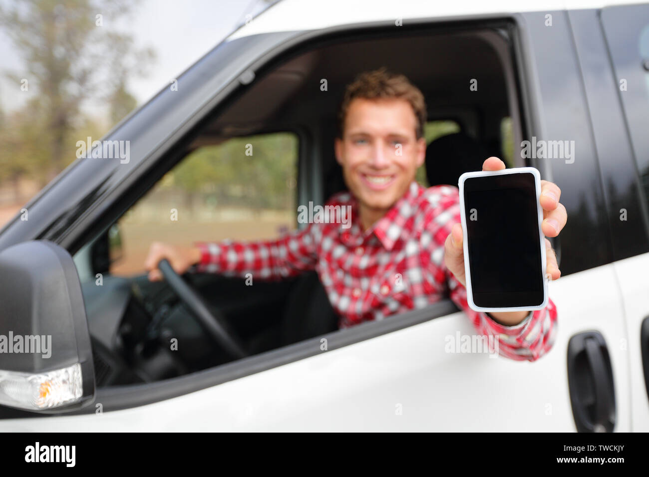 Smart phone uomo in car guida che mostra il display dello smartphone sorridendo felice. Driver maschio utilizzando le app che mostra vuoto nella schermata vuota seduto nel sedile di guida. Focus sul telefono cellulare. Foto Stock