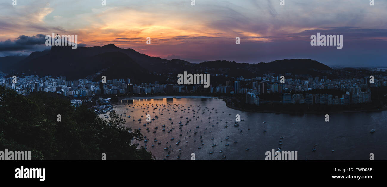 Vista panoramica di Rio de Janeiro al tramonto. La barca si trova nel porto e spiagge piegano attorno alla baia sotto il cristo redentore statua, Brasile Foto Stock