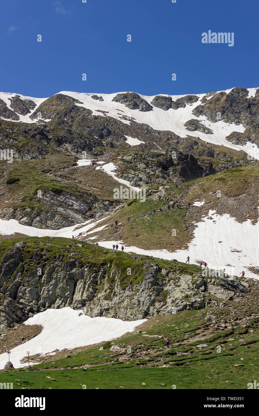 Un folto gruppo di escursionisti salendo la coperta di neve collina su una pista di famosi sette laghi di Rila in Bulgaria in una giornata di sole Foto Stock