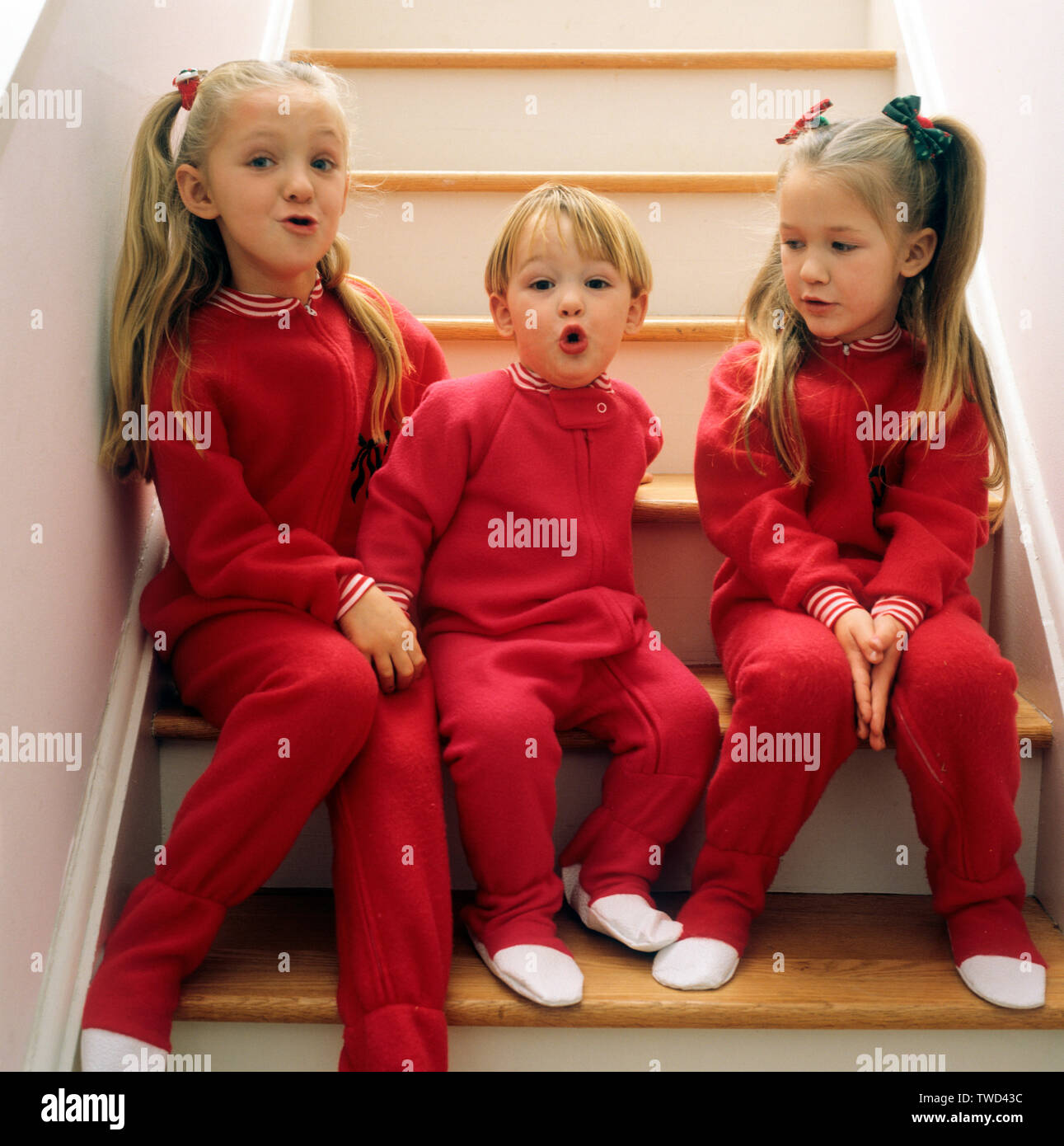 Tre bambini seduti su una scala tutti indossando pigiami rosso Foto Stock