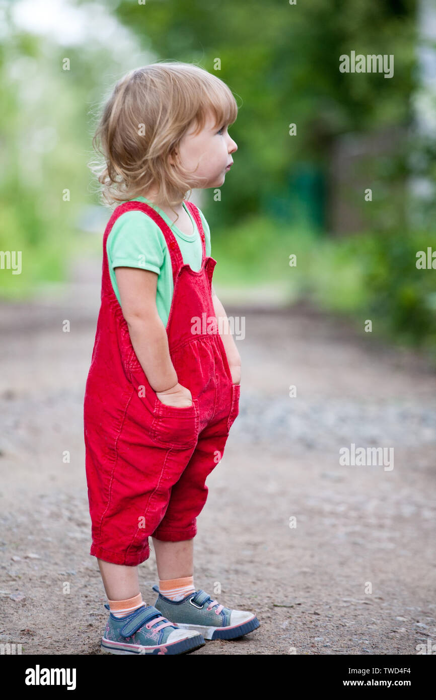 Funny kid ragazza in pantaloni rosso permanente sulla estate sfondo all'aperto Foto Stock