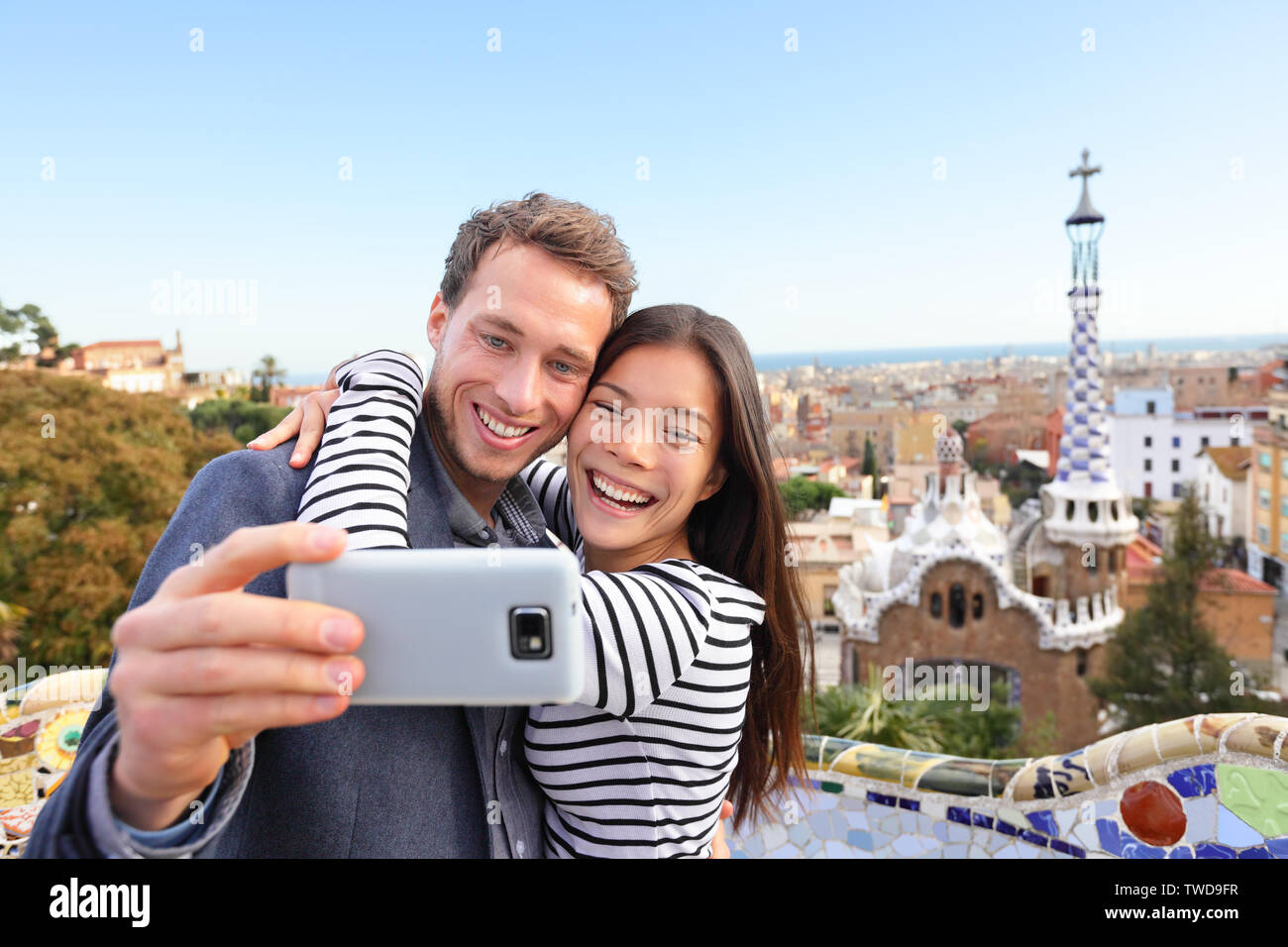 Viaggiare giovane felice parlando selfie autoritratto con lo smartphone nel Parco Guell, Barcelona, Spagna. Giovane e bella multirazziale giovane guardando la telecamera tenendo foto con smart phone sorridente in amore. Foto Stock