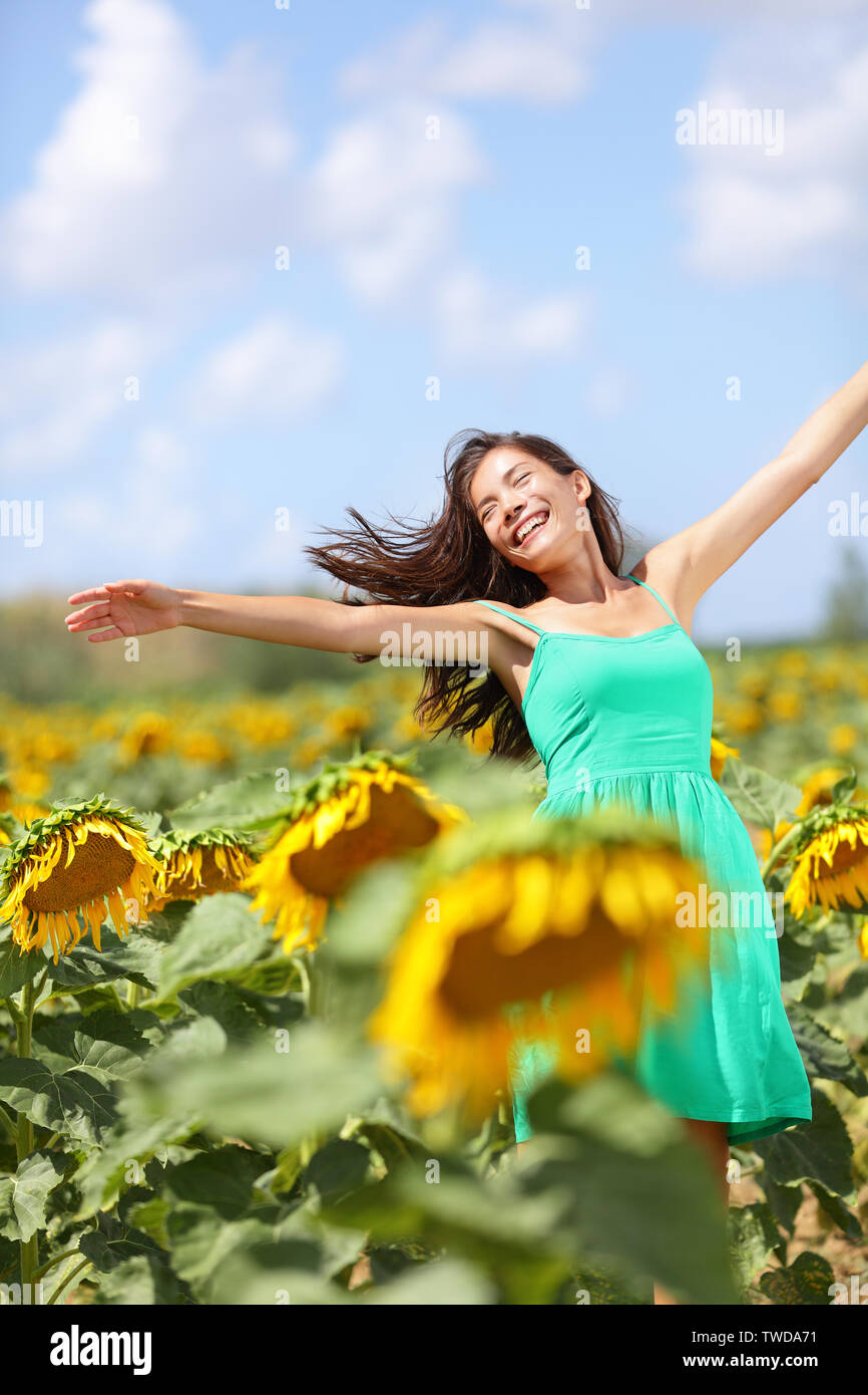 Felice estate spensierata ragazza nel campo di semi di girasole in primavera. Allegro e multirazziale caucasico asiatica giovane donna gioiosa, sorridente con le braccia sollevate verso l'alto. Foto Stock
