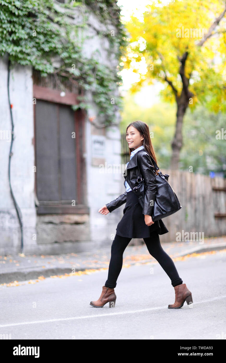 Urban giovane donna camminare in giacca di pelle in città attraversando strade in pieno lunghezza in autunno autunno. Alla moda femminile moderno vivere lo stile di vita della città. Multirazziale asiatici modello caucasico. Foto Stock