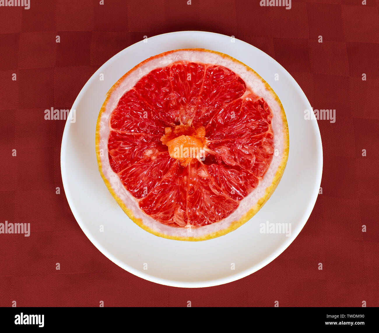 Una metà di un pompelmo su un disco bianco e lo sfondo rosso Foto Stock