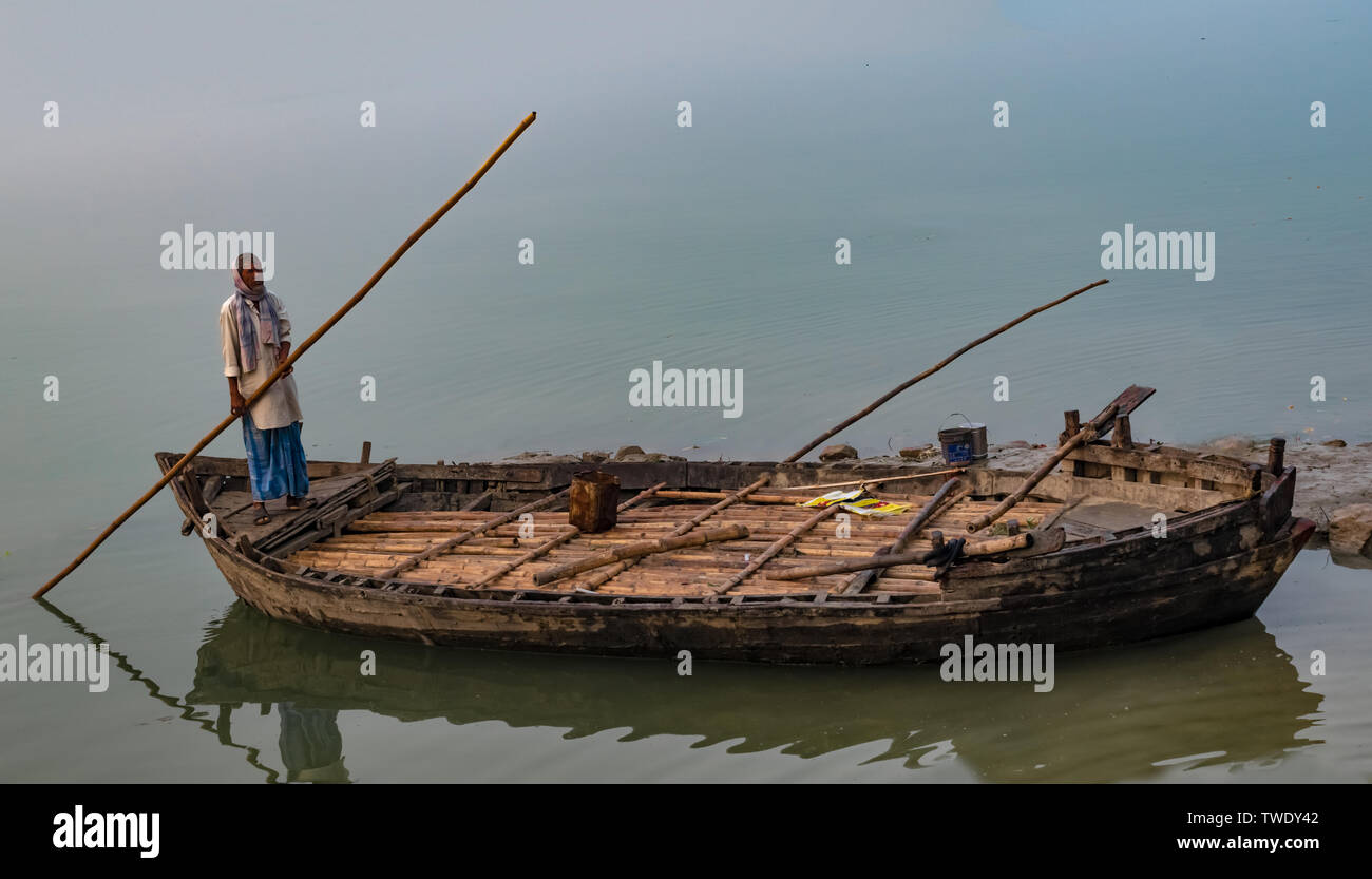 Di mezza età uomo indiano il canottaggio la sua imbarcazione in legno, verso il fiume Gange banca, negli inverni di congelamento dell India del Nord. La visibilità è scarsa a causa della nebbia in inverni. Foto Stock