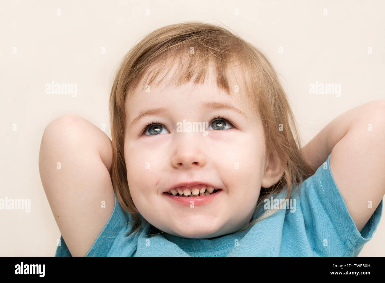 Funny sognante bianco emozionale bambino faccia ragazza closeup sul muro beige background Foto Stock