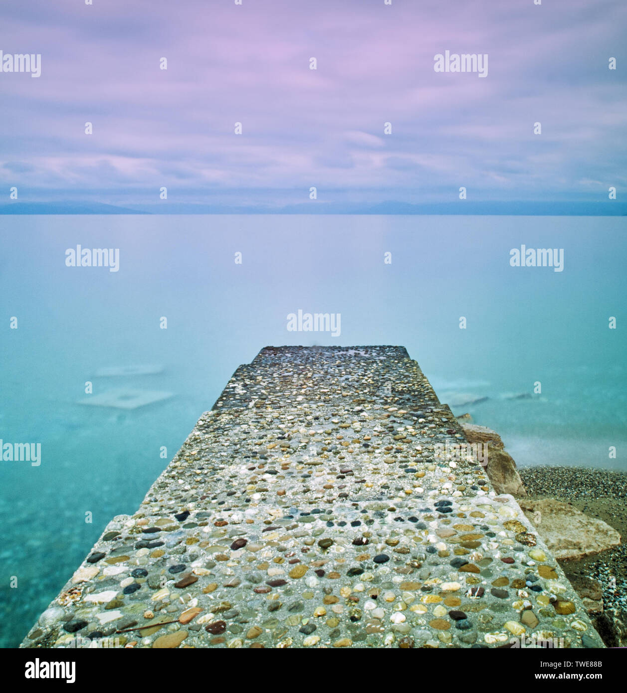 Il molo di pietra che conduce al mare liscio e nuvoloso cielo viola. Foto Stock