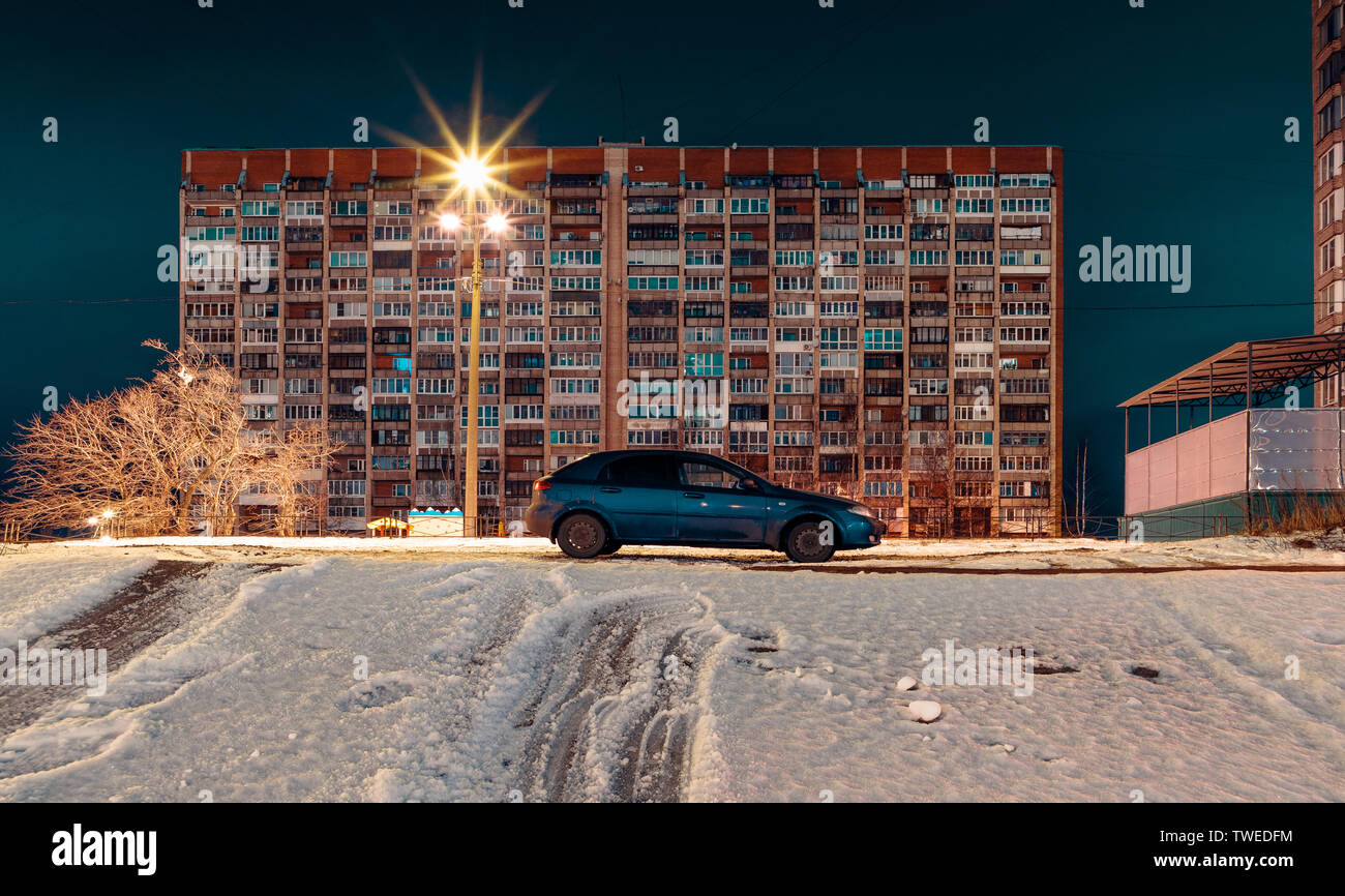 Auto blu sullo sfondo di un edificio a più piani in serata in inverno Foto Stock
