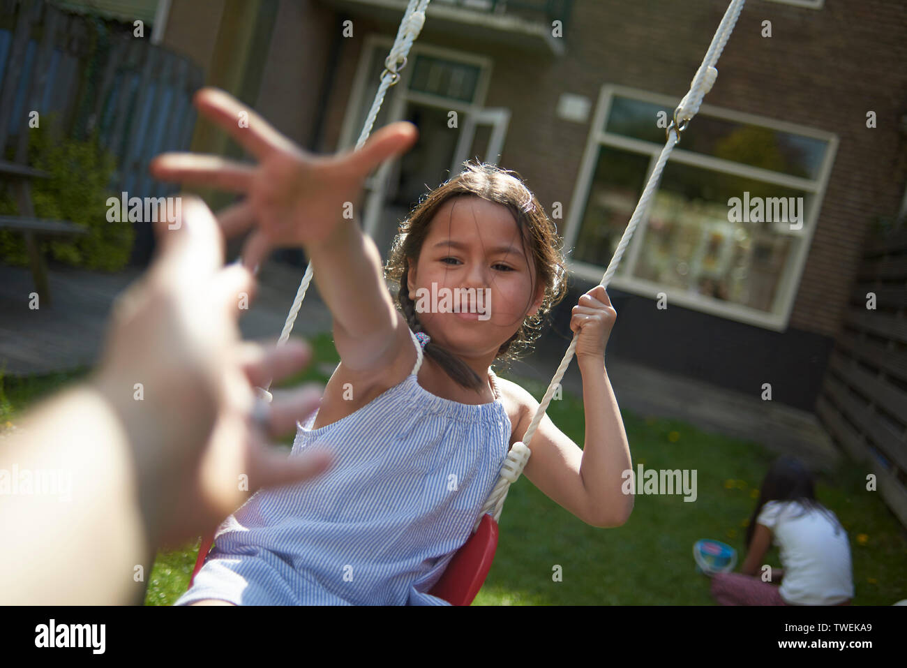 POV di padre a giocare con la sua giovane figlia nel giardino sul retro su un altalena nel sole primaverile Foto Stock