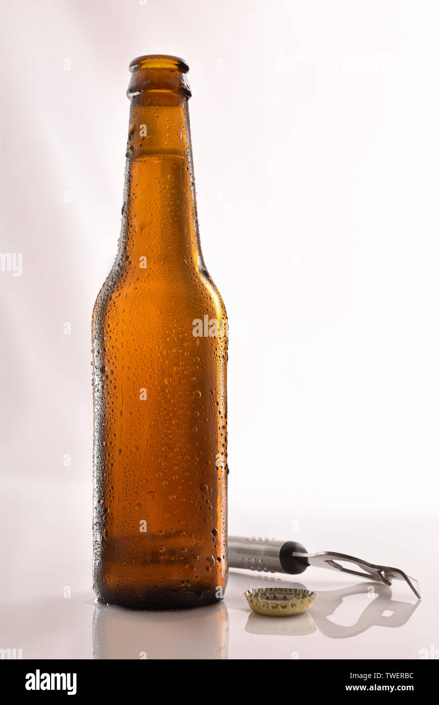 Bottiglia di birra riempita e aperta sul tavolo di vetro e sfondo bianco. Composizione verticale. Vista frontale. Foto Stock