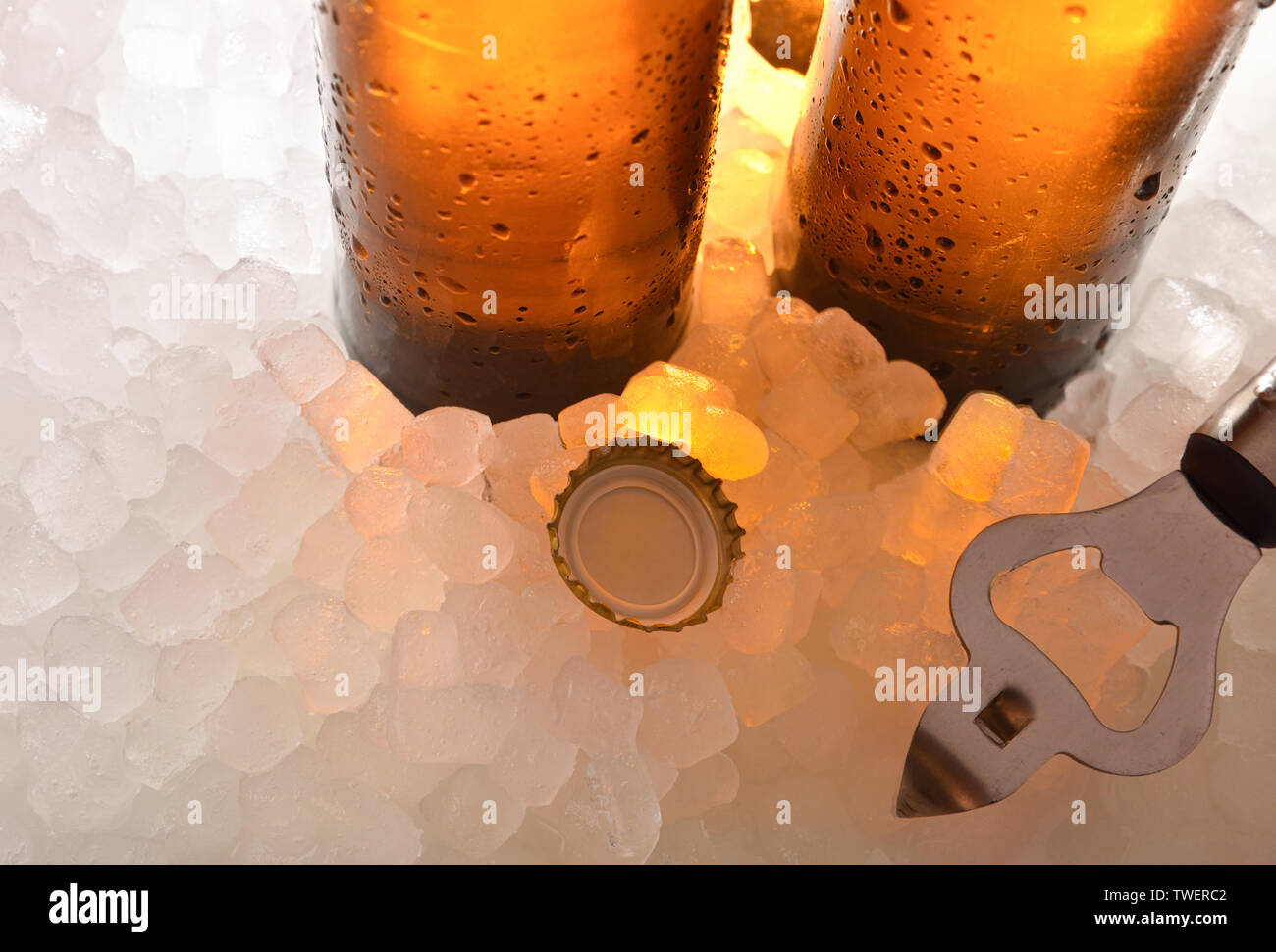 La birra di bottiglie di vetro su ghiaccio con cappuccio e apribottiglie . Composizione orizzontale. Vista in elevazione. Foto Stock