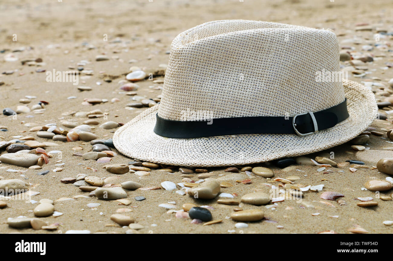 Chiusura del cappello di paglia su una spiaggia sabbiosa e di pietra grigia spiaggia. Estate vacanze. Concetto di sfondo di viaggio. Appartamento di laici e di spazio copia. Foto Stock