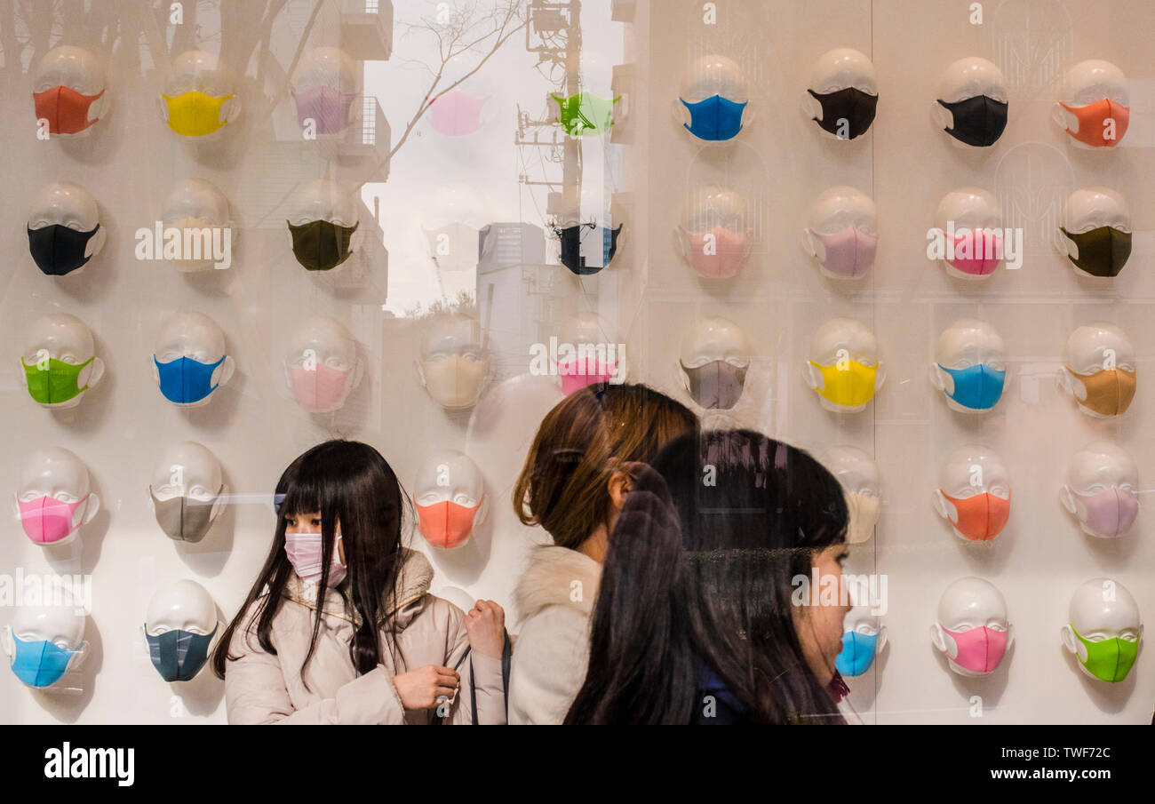 Tre donne in un negozio visto attraverso la finestra con ampia selezione di colorate maschere di inquinamento sul display nell'area di Omotesando a Tokyo in Giappone. Foto Stock