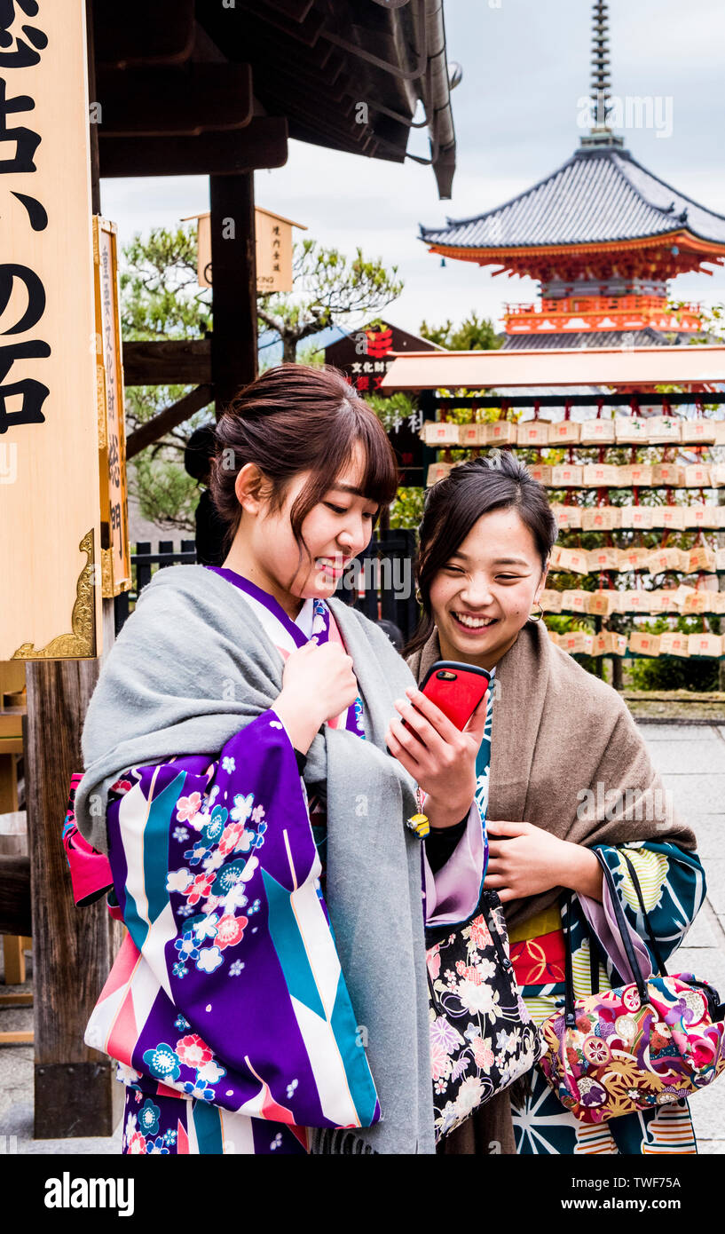 Due donne in abito tradizionale guardando smartphone e sorridente a Kiyomizu-dera tempio di Kyoto in Giappone. Foto Stock