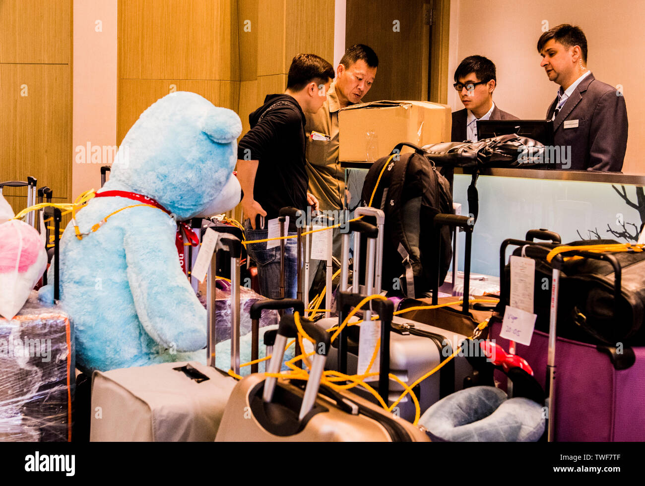 Passeggeri in piedi al check point con righe di bagagli tra cui una molto grande blu orsacchiotto dietro di loro a Kowloon in Hong Kong. Foto Stock