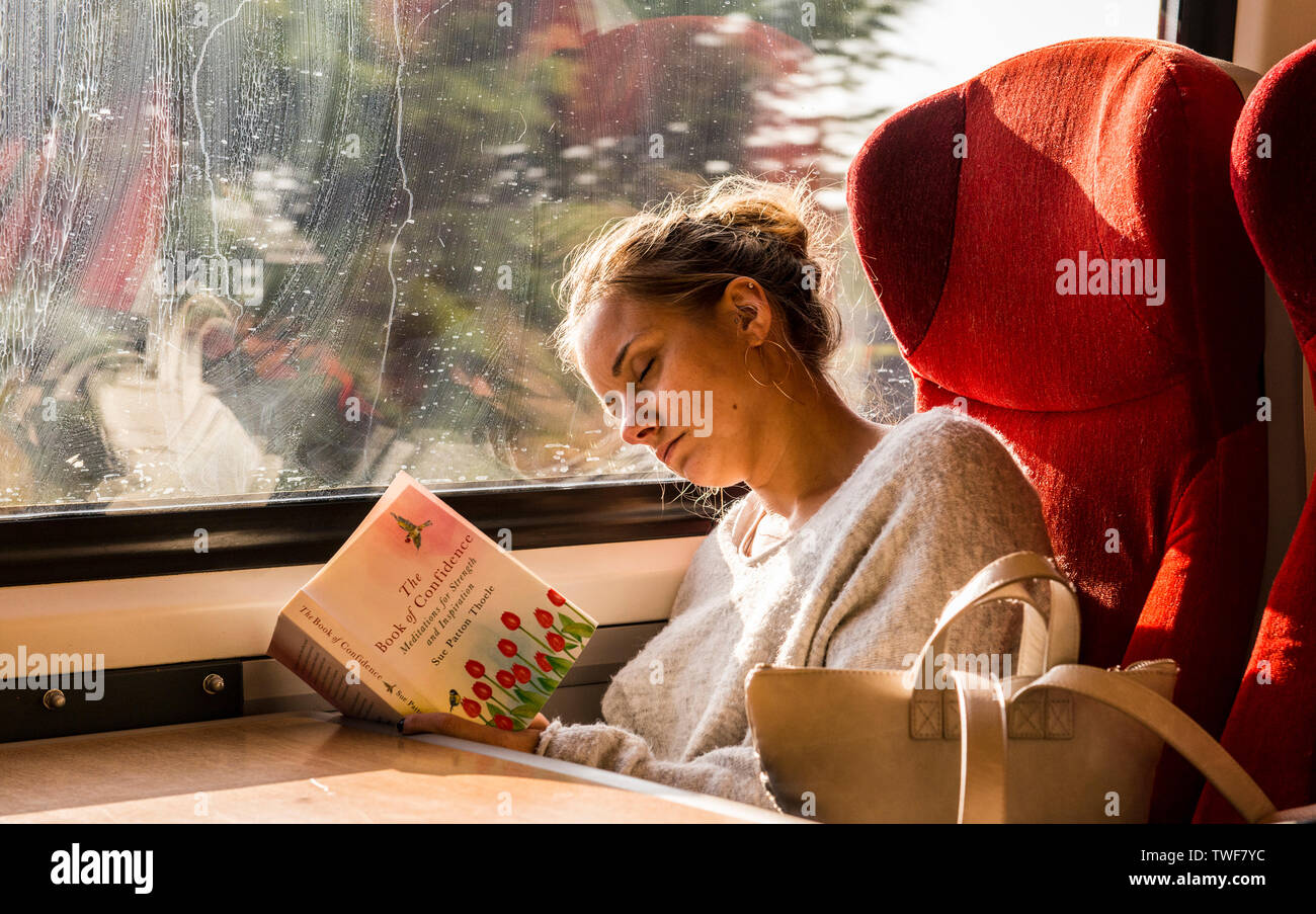 Donna sul treno seduto accanto alla finestra e dormire mentre tiene libro aperto cercando di leggere. Foto Stock