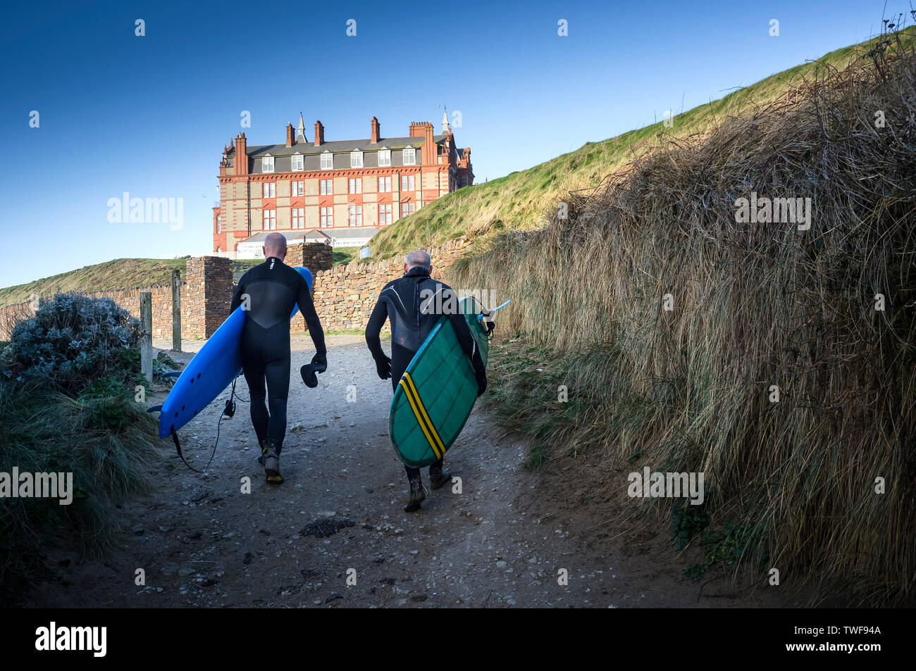 Coppia di surfers che trasportano le loro tavole da surf a piedi fino al promontorio Hotel a Fistral a Newquay in Cornovaglia. Foto Stock