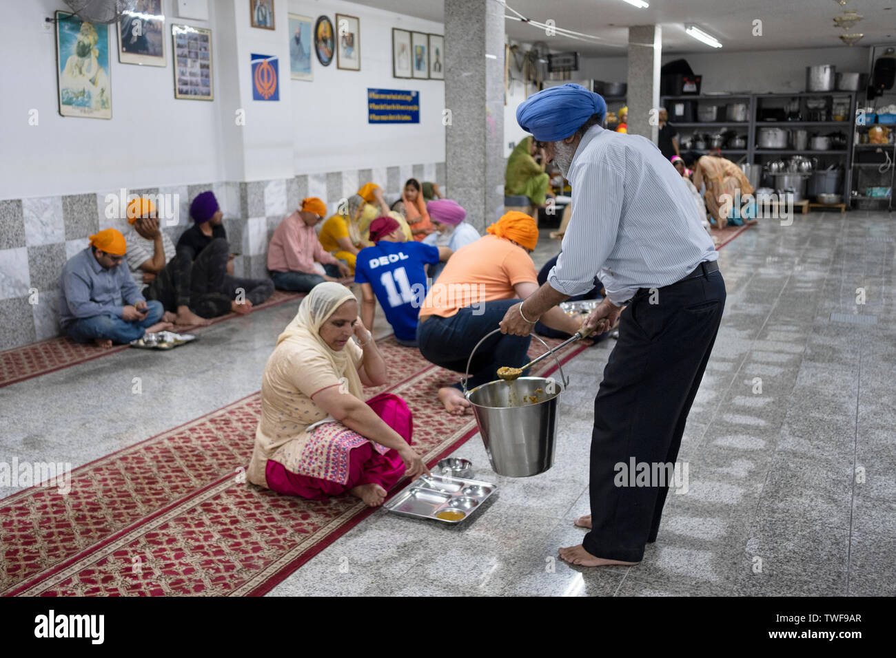 Un uomo Sikh volontariato nel langar (comunità libera cucina) alimenta un compagno adoratore nel lavaggio, Queens, a New York City. Foto Stock