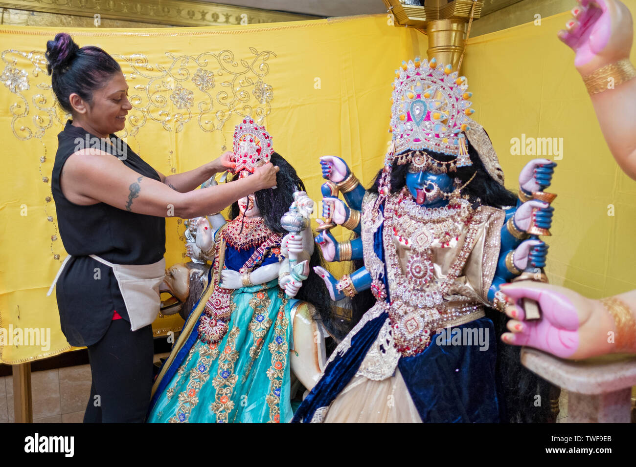 Come parte di un ringraziamento rituale, un devoto Hindu progettato e installato nuovi vestiti sul tempio statue di divinità. In Ozone Park, Queens, NYC Foto Stock
